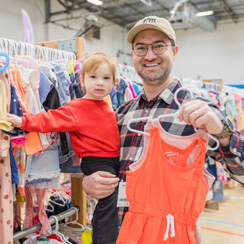 A dad holds his daughter and clothes as they shop their local JBF sale.