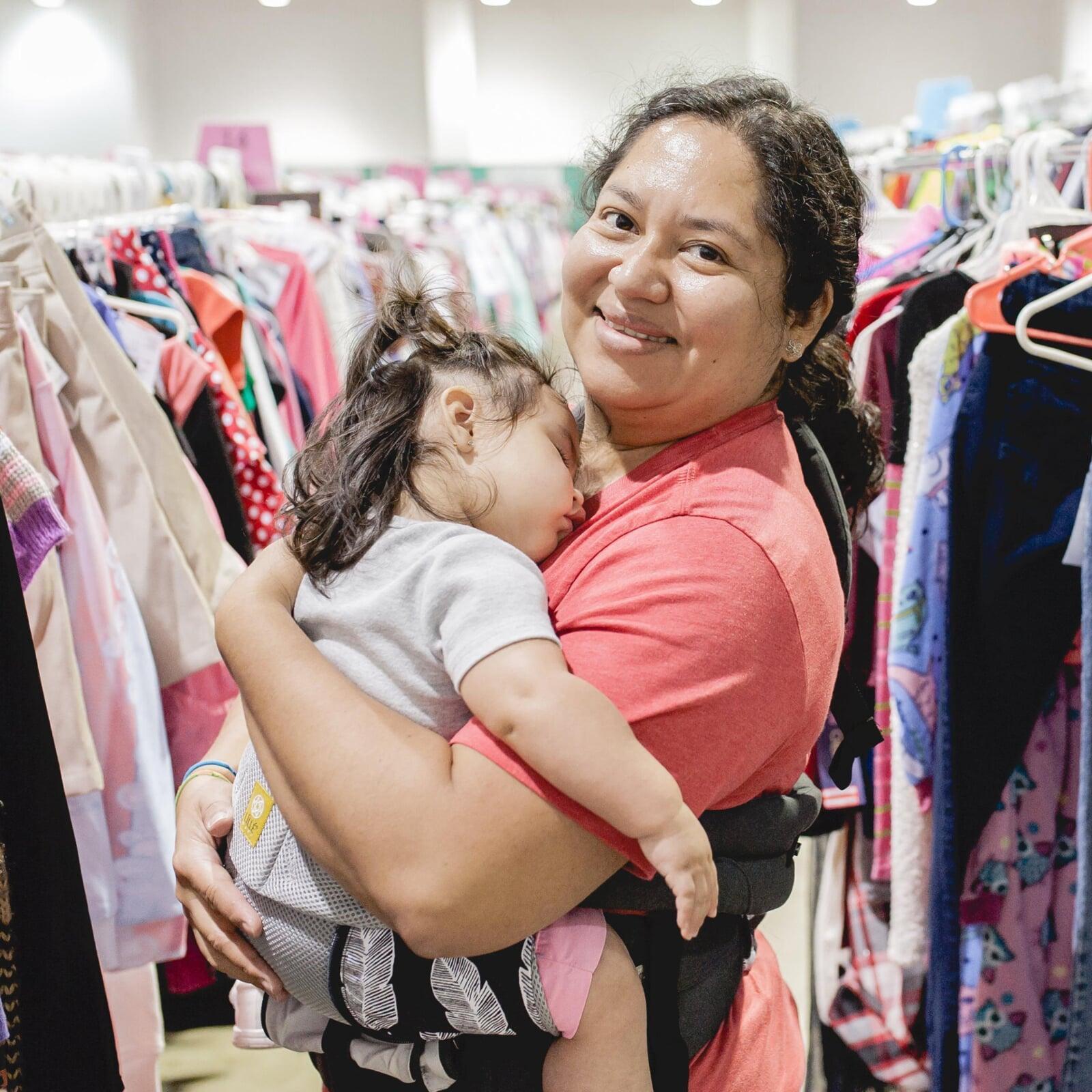 Mom holds daughter who is sleeping in her arms while she shops the local JBF sale.