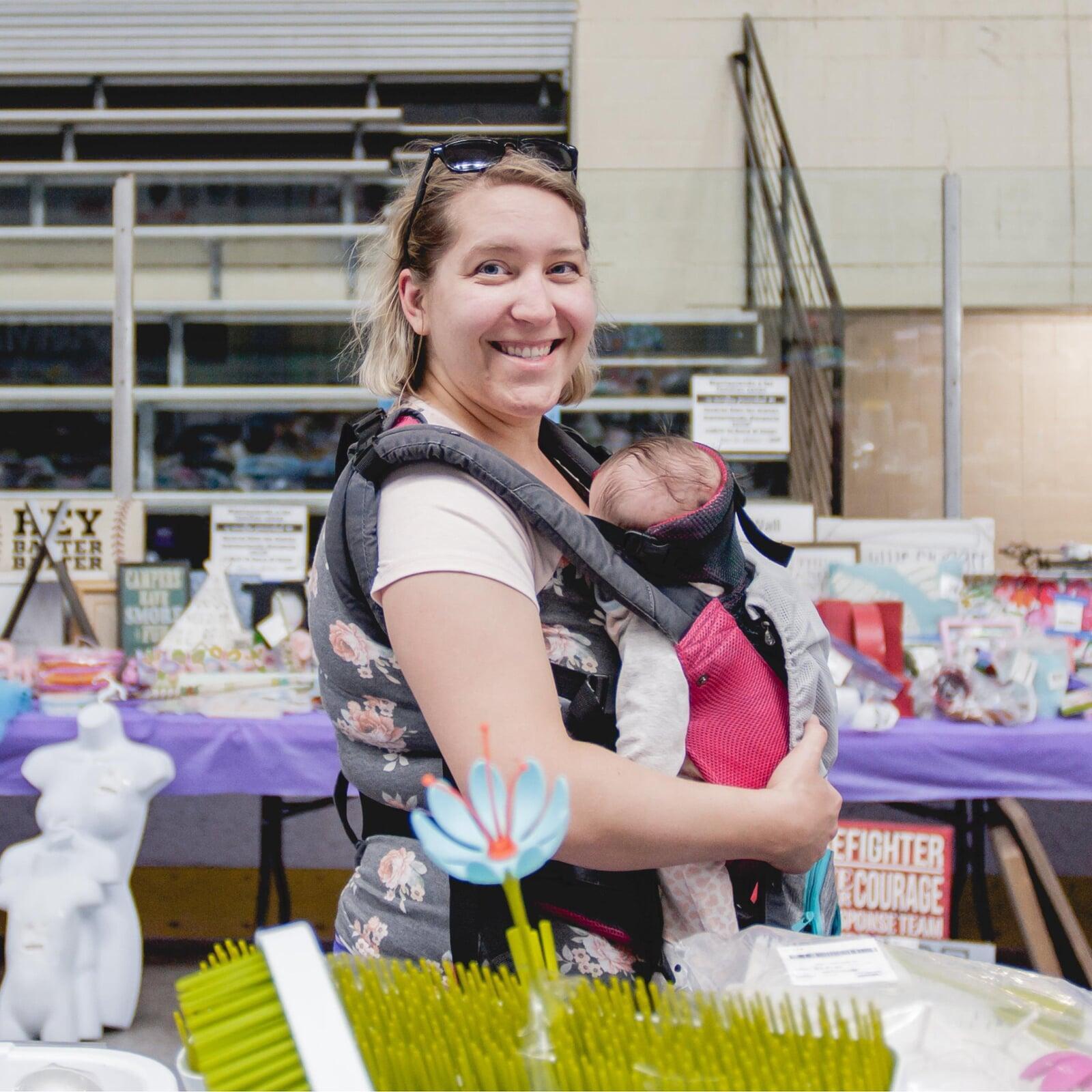 Mom holding baby in carrier shopping for her family at the local JBF sale