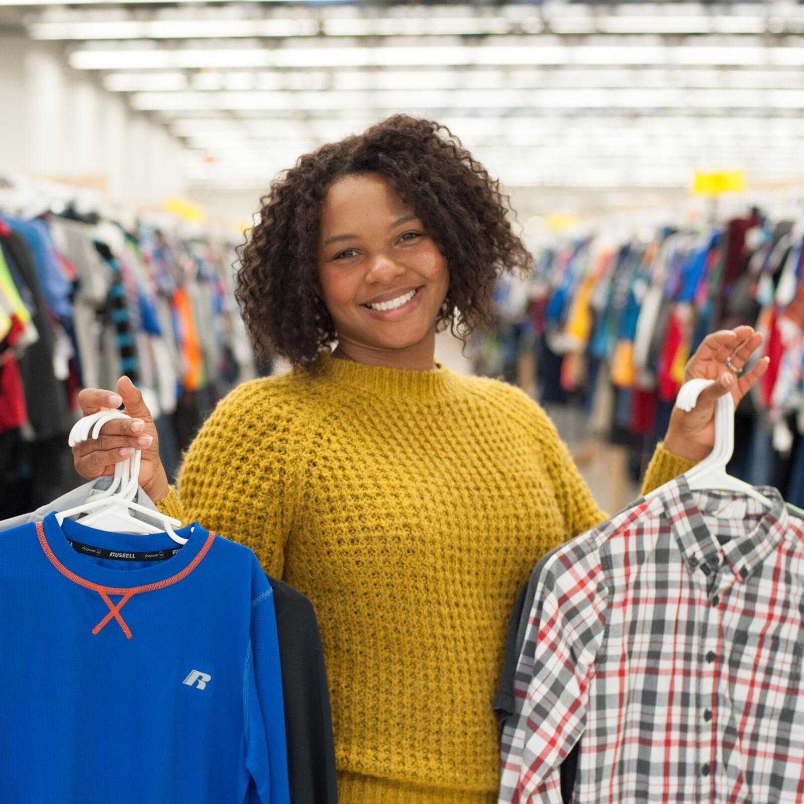 Beautiful mom holds two boys tops—one in each hand—as she shops the deals at her local sale.